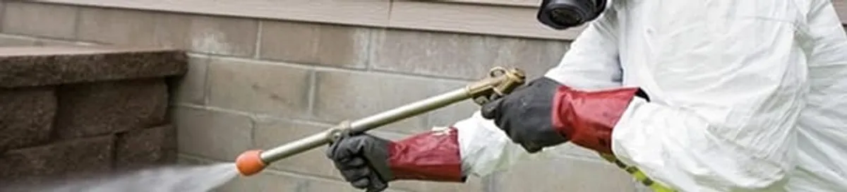 Pest control technician applying exterior insect treatment along a home foundation in Phoenix, AZ