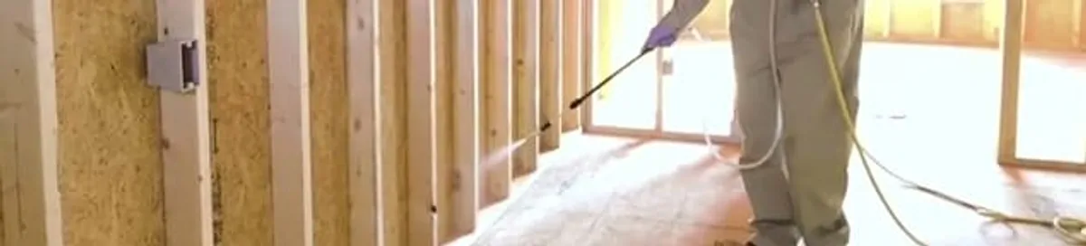 Termite treatment technician applying spray along framing and unfinished walls in Phoenix, AZ